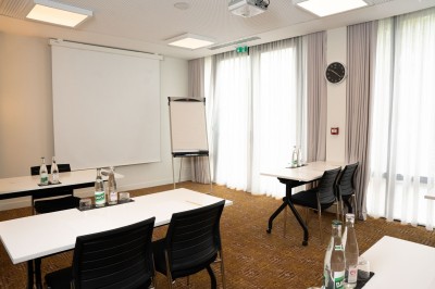 Miniature Location salle Blagnac (Haute-Garonne) - Osko #3 Chambre d'hôtel avec deux lits simples, un fauteuil, un bureau, une lampe et une grande fenêtre avec rideaux.