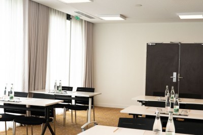 Miniature Location salle Blagnac (Haute-Garonne) - Osko #17 Chambre d'hôtel avec deux lits simples, un fauteuil, un bureau, une lampe et une grande fenêtre avec rideaux.