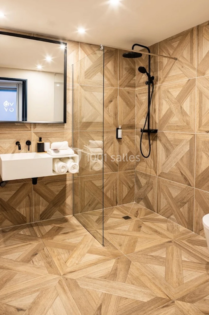 Salle de bain moderne avec douche à l'italienne, carrelage effet bois, lavabo suspendu et miroir rectangulaire.
