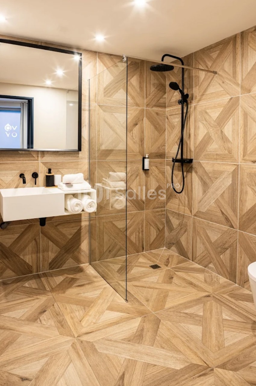 Salle de bain moderne avec douche à l'italienne, carrelage effet bois, lavabo suspendu et miroir rectangulaire.