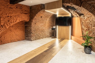 Salle moderne avec murs en briques apparentes, sol en bois et carrelage, écran mural et plante en pot.