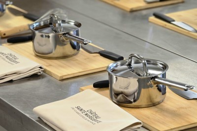 Casseroles en inox posées sur des planches en bois avec couteaux et torchons, disposés sur un plan de travail.