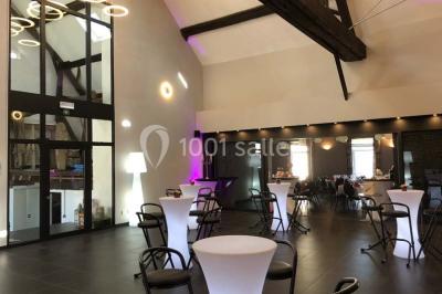 Tente blanche avec toit pointu et bordure rouge installée dans un jardin arboré, entourée de tables et chaises.