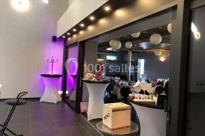 Tente blanche avec toit pointu et bordure rouge installée dans un jardin arboré, entourée de tables et chaises.