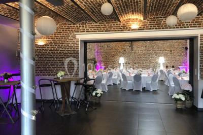 Tente blanche avec toit pointu et bordure rouge installée dans un jardin arboré, entourée de tables et chaises.