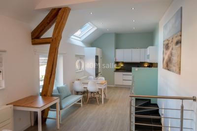 Tente blanche avec toit pointu et bordure rouge installée dans un jardin arboré, entourée de tables et chaises.