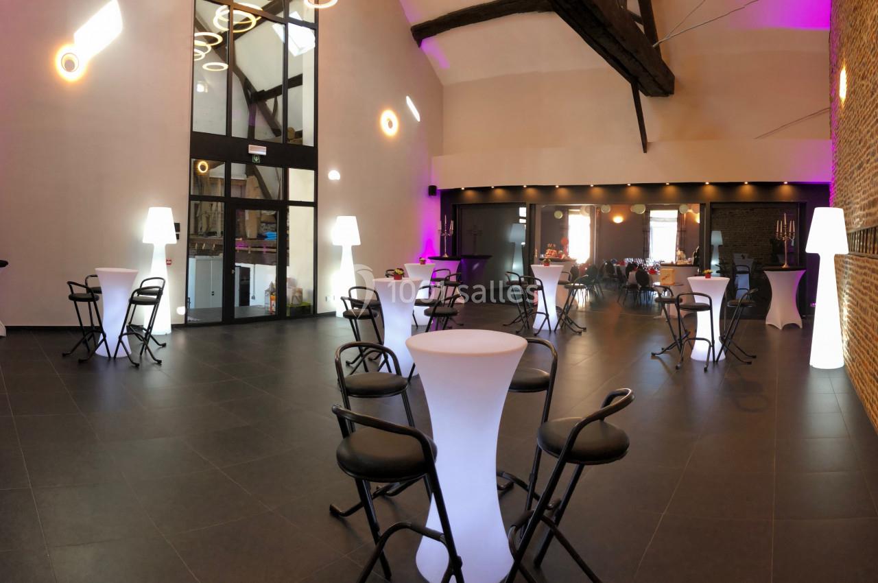 Salle de réception moderne avec murs en briques, tables hautes, chaises noires et éclairage tamisé.