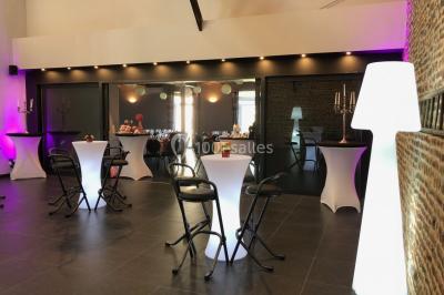 Tente blanche avec toit pointu et bordure rouge installée dans un jardin arboré, entourée de tables et chaises.