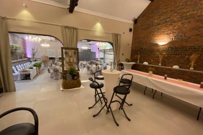 Tente blanche avec toit pointu et bordure rouge installée dans un jardin arboré, entourée de tables et chaises.