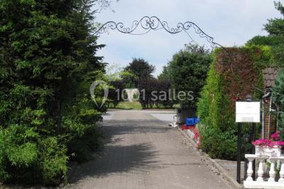 Tente blanche avec toit pointu et bordure rouge installée dans un jardin arboré, entourée de tables et chaises.
