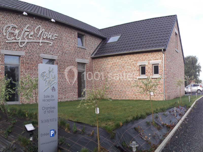 Bâtiment en briques rouges avec un panneau indiquant une salle de réception et des chambres d'hôtes, entouré d'un jardin.