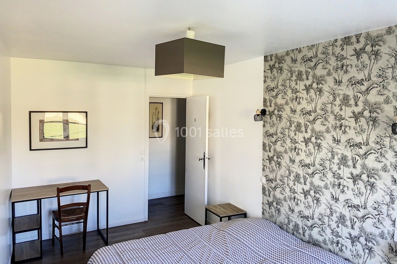 Chambre lumineuse avec lit, bureau en bois, chaise et mur décoré d'un papier peint à motifs végétaux.