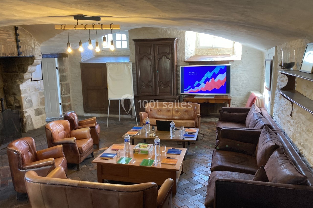 Salle de réunion rustique avec fauteuils en cuir, table basse, écran affichant un graphique et tableau blanc.