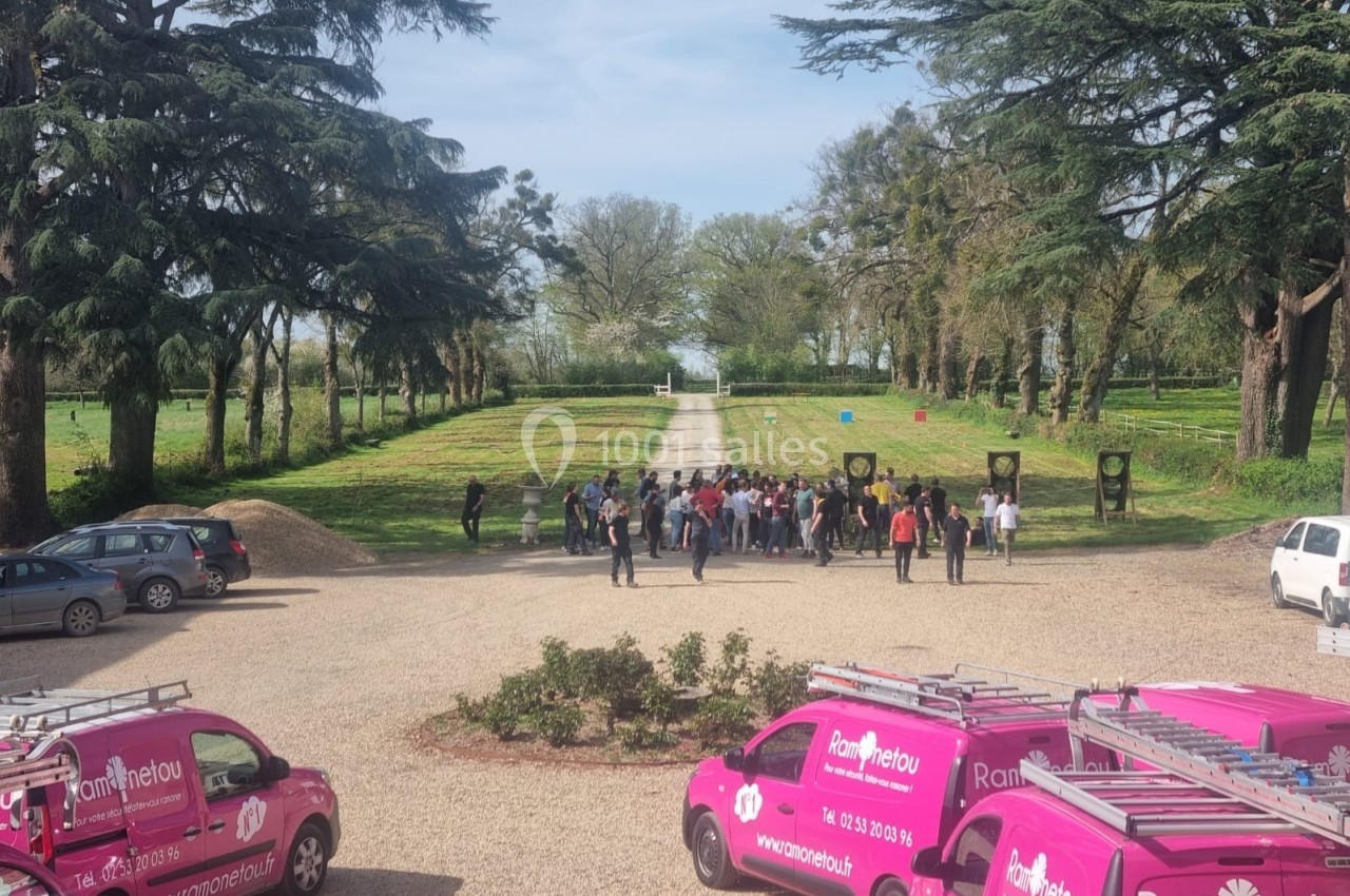 Un groupe de personnes rassemblé en plein air près d'une allée bordée d'arbres, avec des véhicules roses au premier plan.
