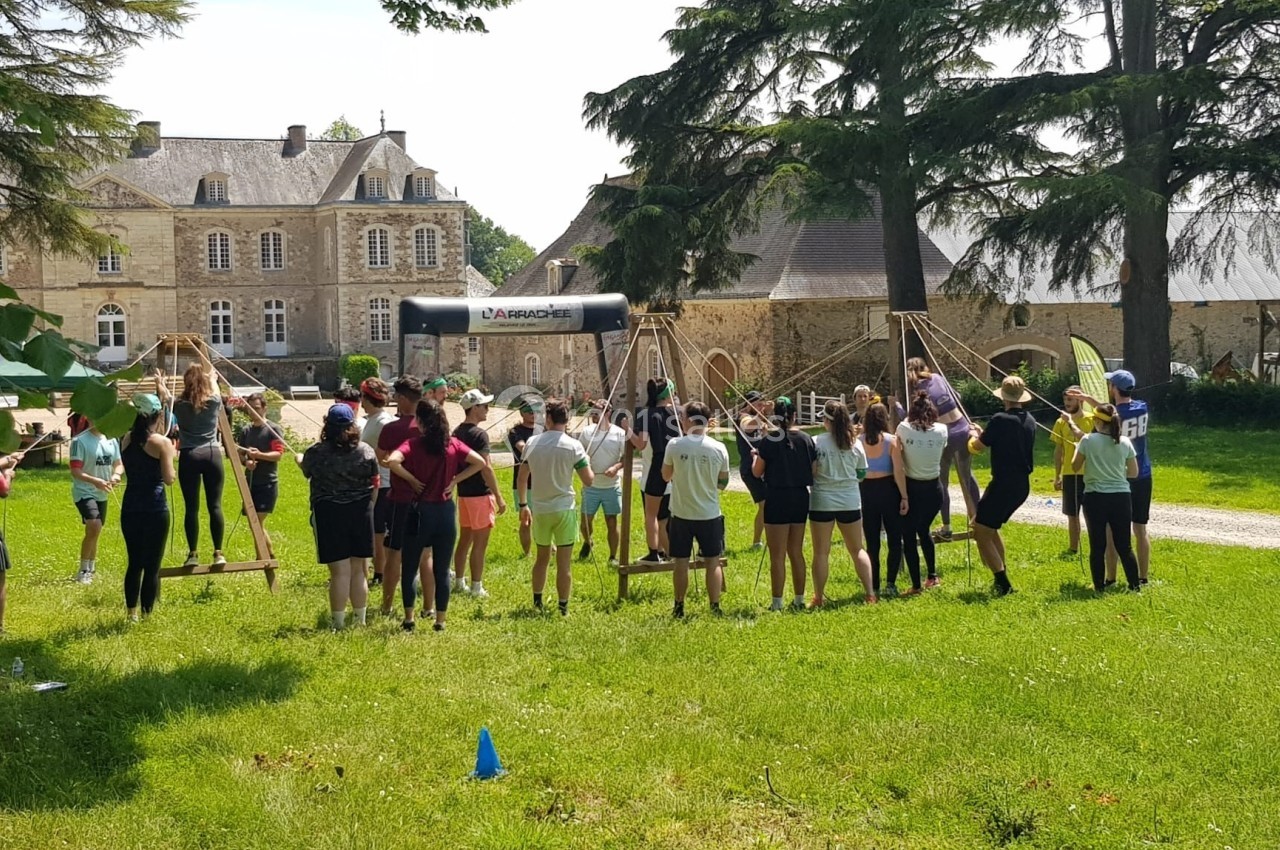 Un groupe de personnes participe à une activité en plein air devant un bâtiment ancien entouré de verdure.