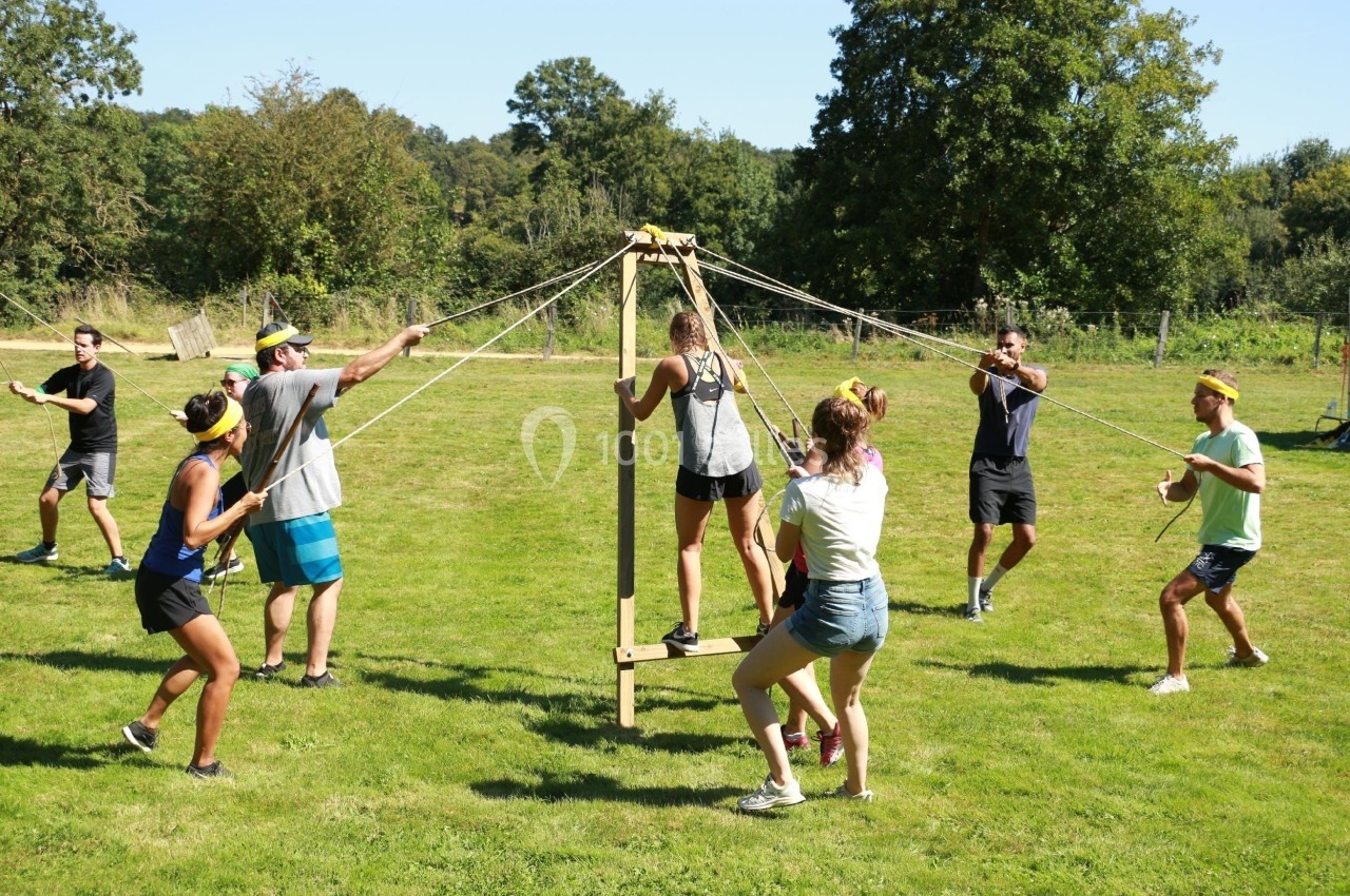 Des personnes participent à une activité collaborative en plein air, manipulant des cordes pour équilibrer une structure en…