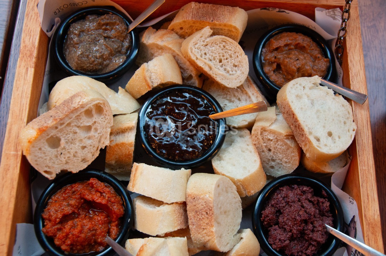 Plateau en bois avec tranches de pain et cinq coupes de pâtes à tartiner sucrées et salées.