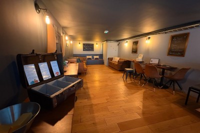 Salle chaleureuse avec parquet en bois, tables, chaises, canapés et éclairage tamisé.