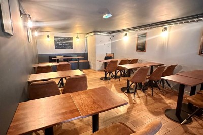 Salle chaleureuse avec parquet en bois, tables, chaises, canapés et éclairage tamisé.
