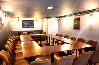 Salle chaleureuse avec parquet en bois, tables, chaises, canapés et éclairage tamisé.