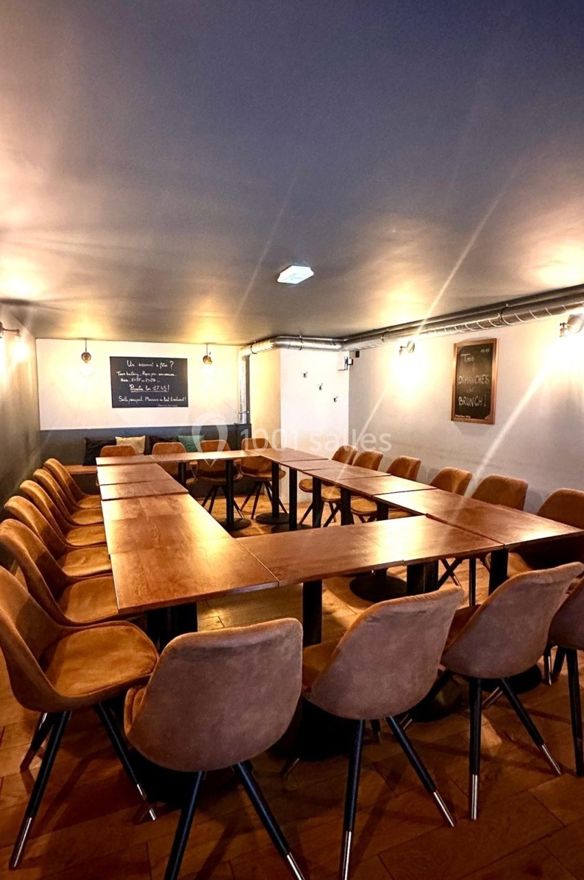 Salle de réunion avec une grande table en bois en forme de U, entourée de chaises en cuir marron.