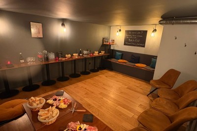 Salle chaleureuse avec parquet en bois, tables, chaises, canapés et éclairage tamisé.