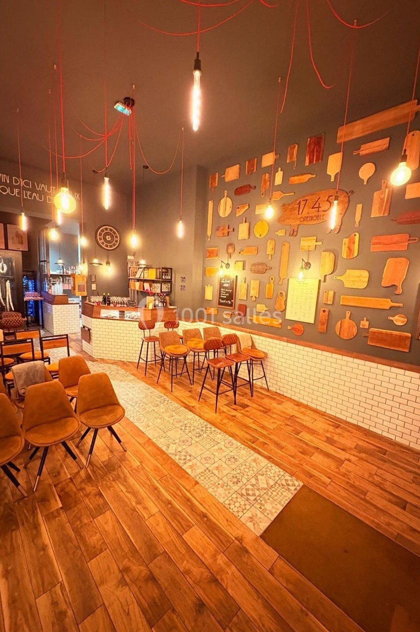 Salle de restaurant chaleureuse avec parquet, chaises en velours, murs décorés de planches en bois et éclairage suspendu.