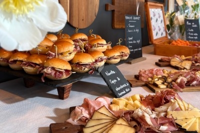 Plateau de mini-burgers au jambon cru et planches de charcuterie et fromages sur une table de buffet.