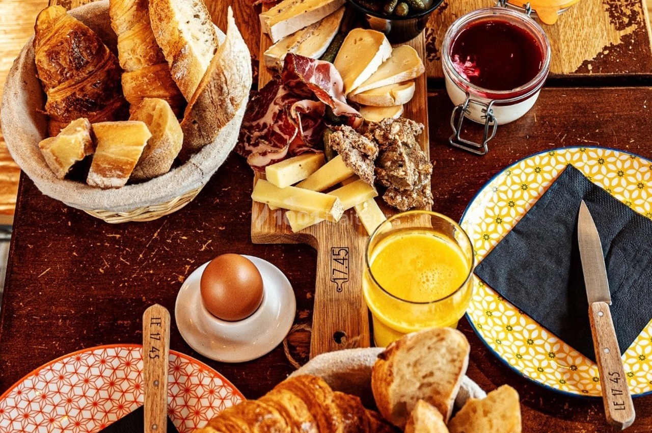 Petit-déjeuner composé de viennoiseries, pain, charcuterie, fromages, œuf, jus d’orange, confiture et cornichons sur une…