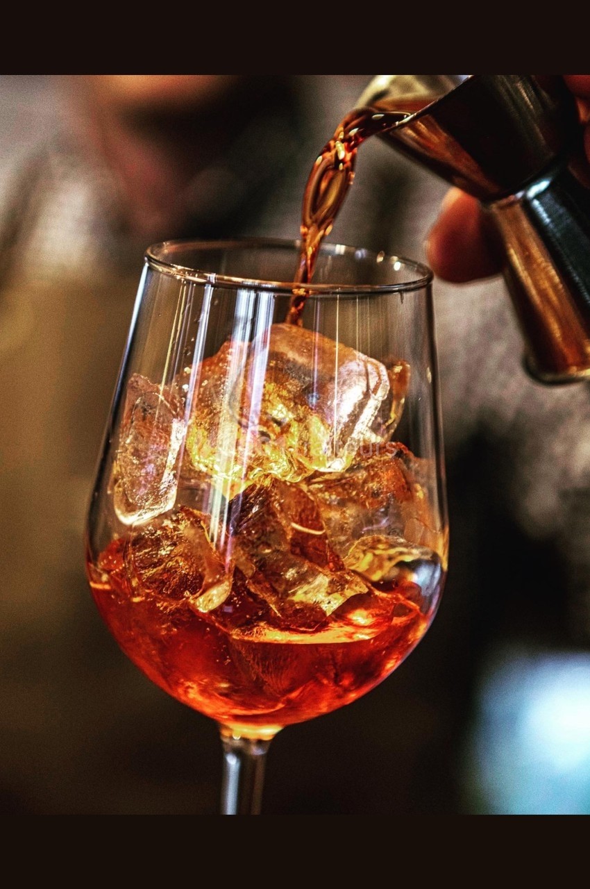 Versement d'une boisson ambrée dans un verre à pied rempli de glaçons, avec un fond flou.