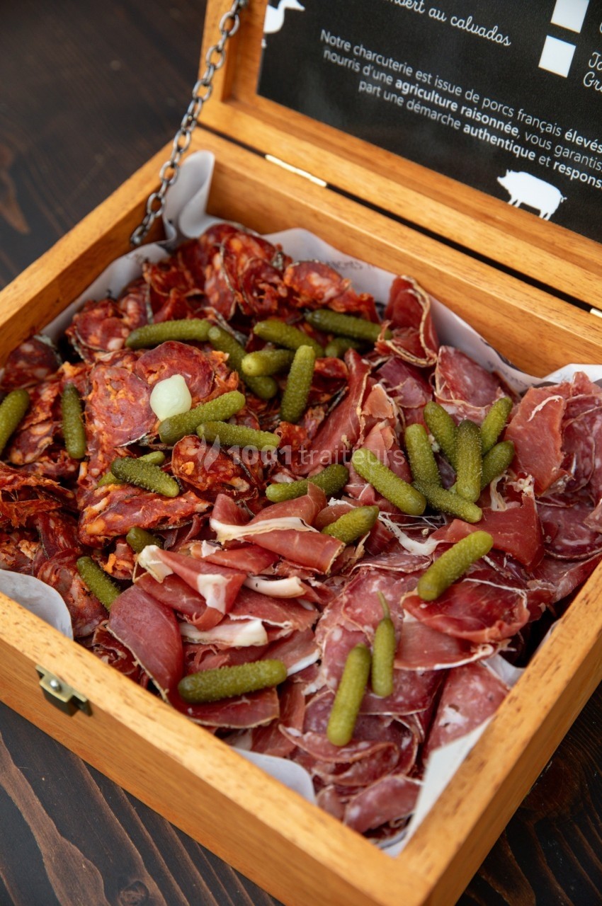 Plateau en bois contenant un assortiment de charcuteries et de cornichons, présenté sur du papier blanc.