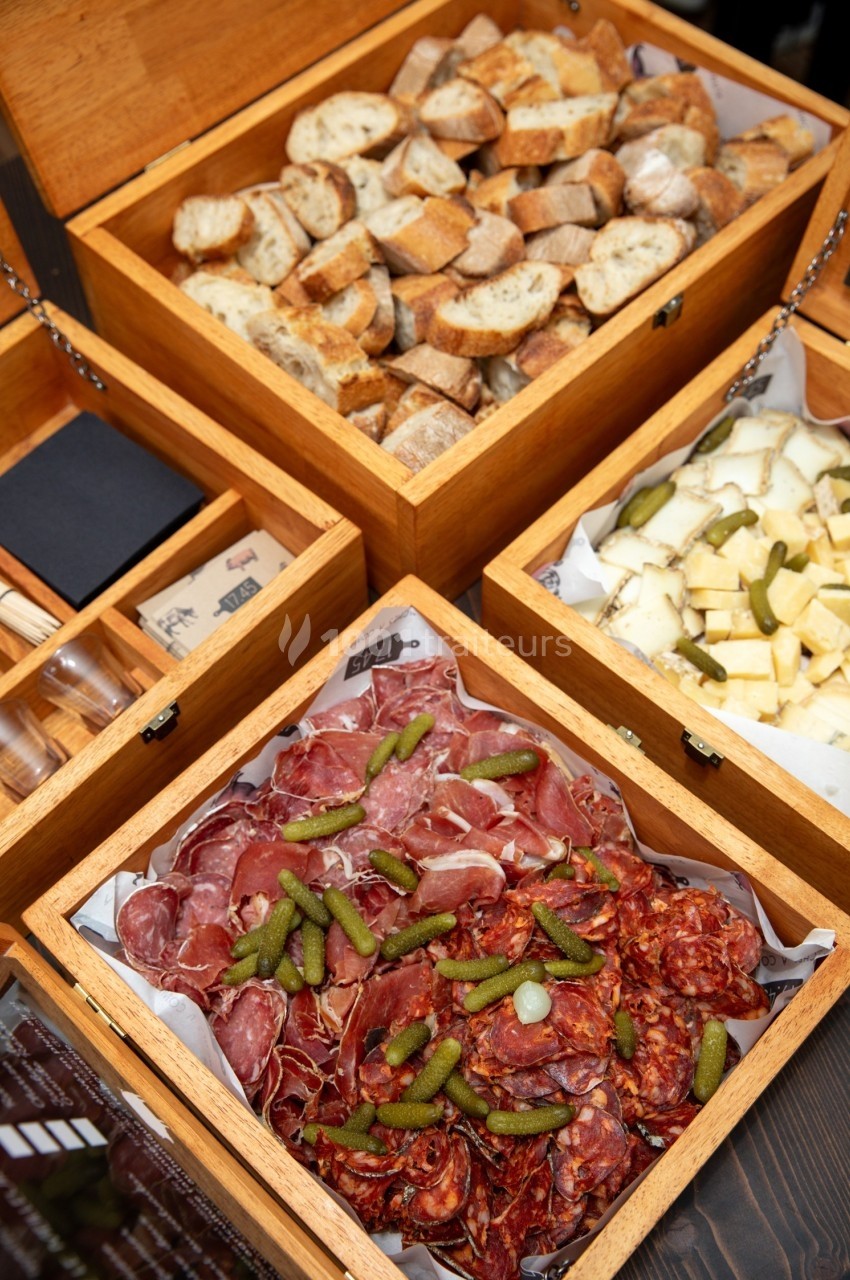 Plateaux en bois contenant du pain, des morceaux de fromage, de la charcuterie et des cornichons.