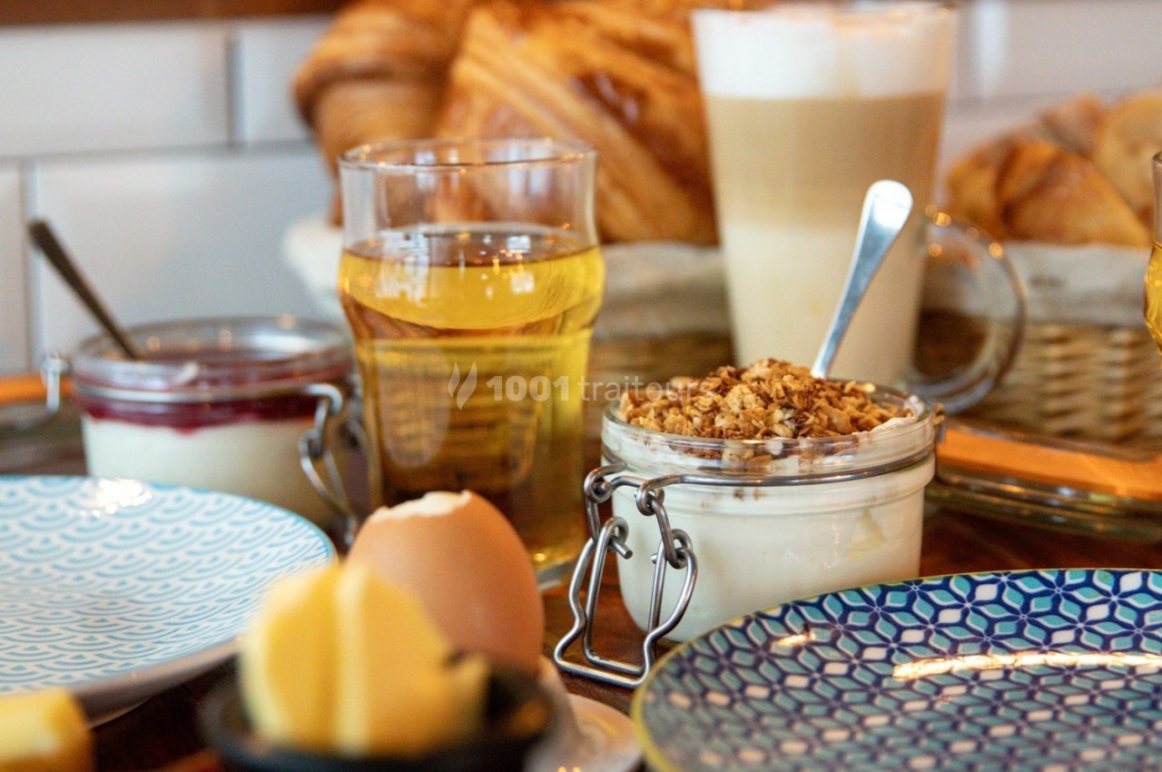 Petit-déjeuner composé de yaourt au granola, jus, café, croissants et œuf à la coque sur une table en bois.