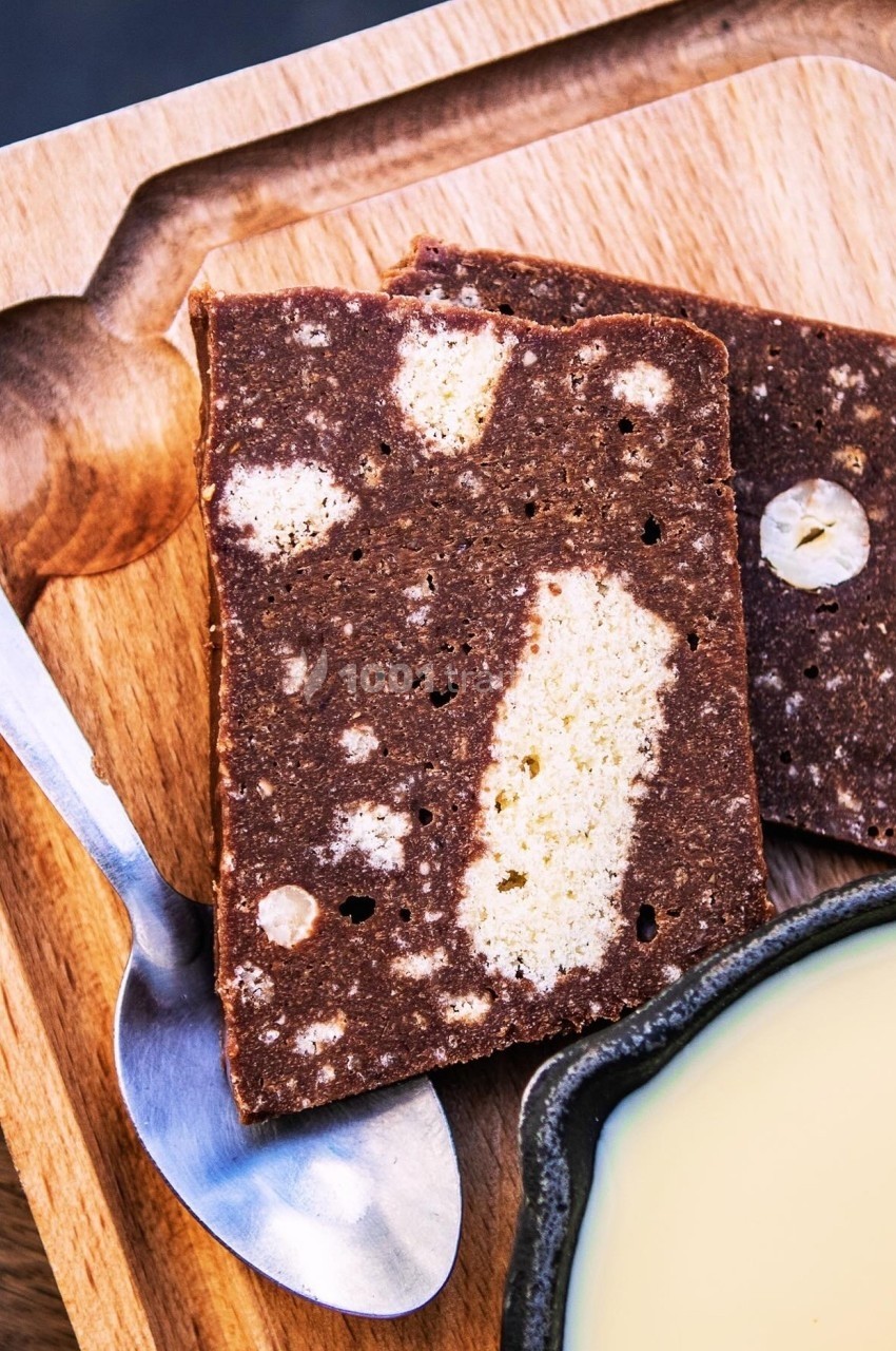 Tranches de gâteau marbré au chocolat et à la vanille sur une planche en bois, avec une cuillère et un bol de sauce.