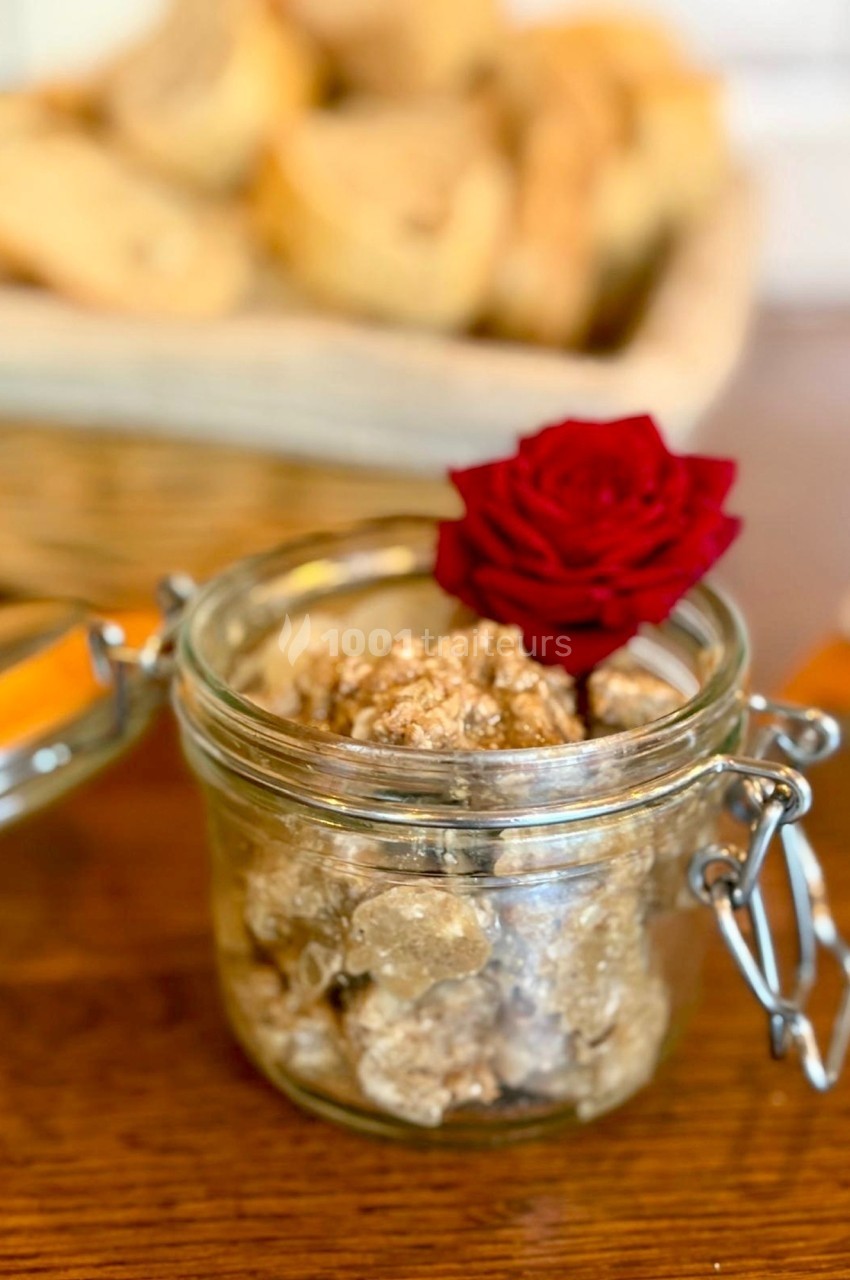 Bocal en verre ouvert contenant des truffes, décoré d'une rose rouge, avec des tranches de pain en arrière-plan.
