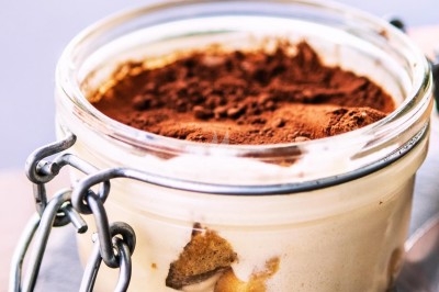 Dessert tiramisu en verrine avec une couche de cacao en poudre sur le dessus, posé sur une ardoise noire.