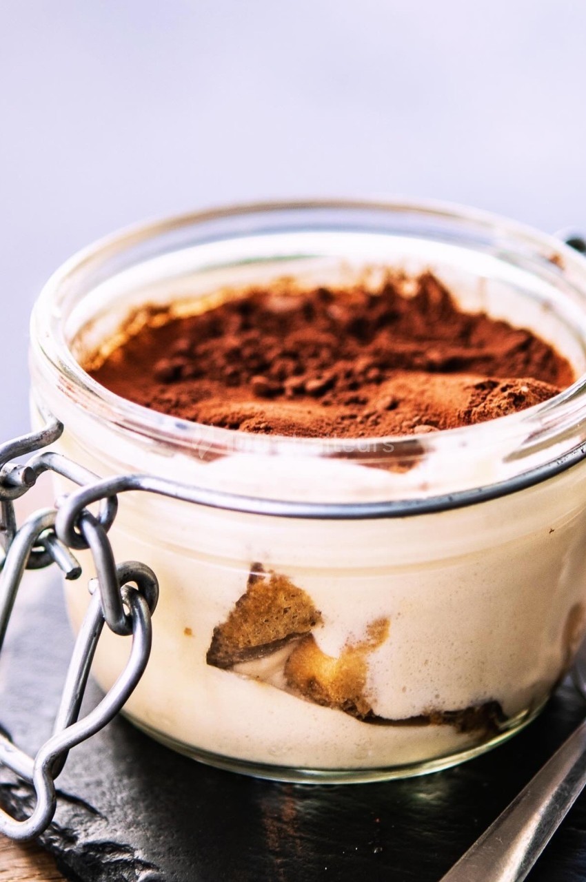Dessert tiramisu en verrine avec une couche de cacao en poudre sur le dessus, posé sur une ardoise noire.