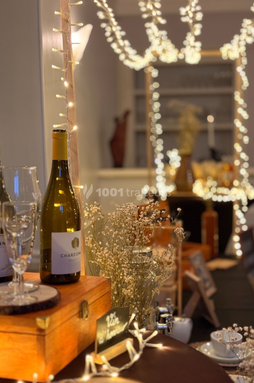 Bouteille de vin blanc et verres sur une table décorée de guirlandes lumineuses et de fleurs séchées.