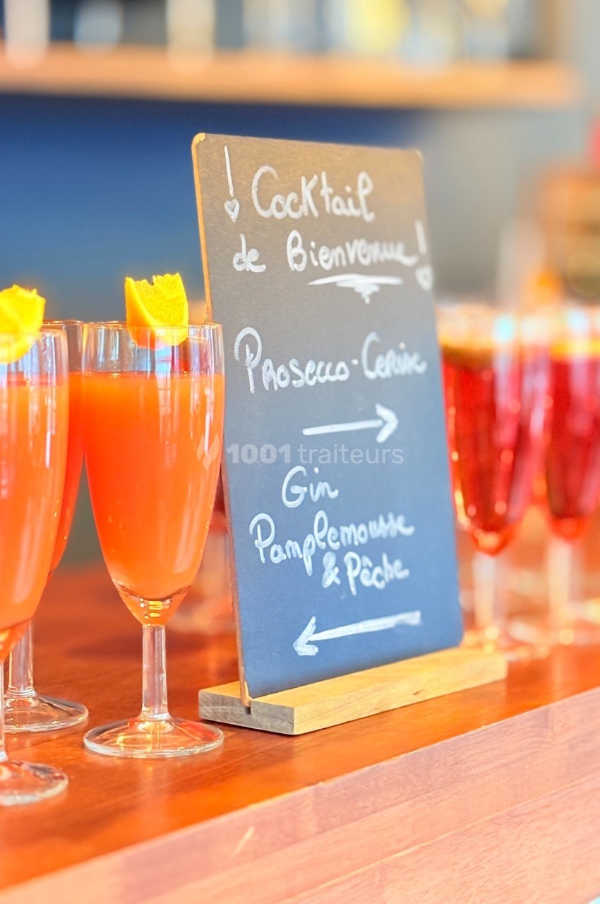 Ardoise indiquant deux choix de cocktails, avec des verres remplis de boissons colorées garnies d'écorces d'orange.