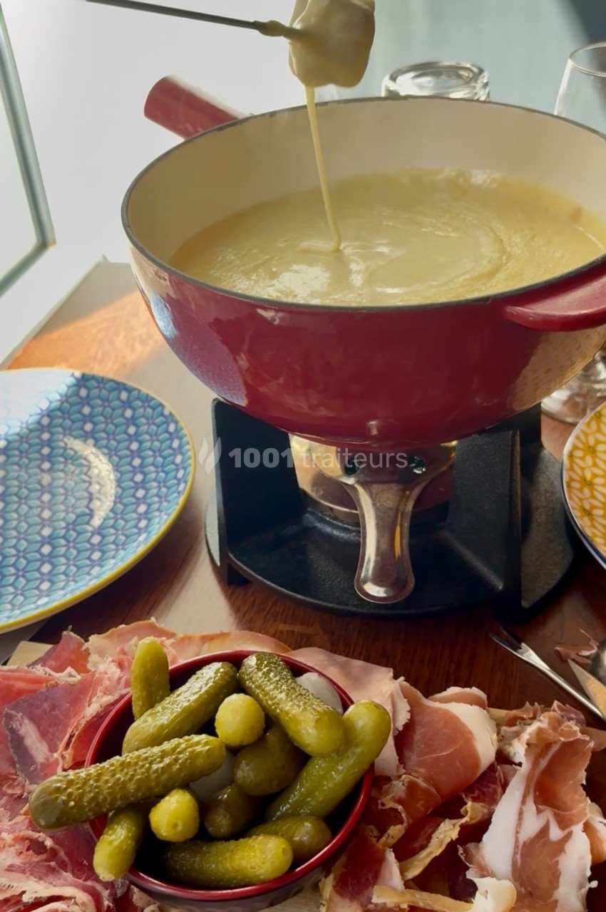 Caquelon de fondue au fromage avec cornichons, charcuterie et assiettes colorées sur une table en bois.