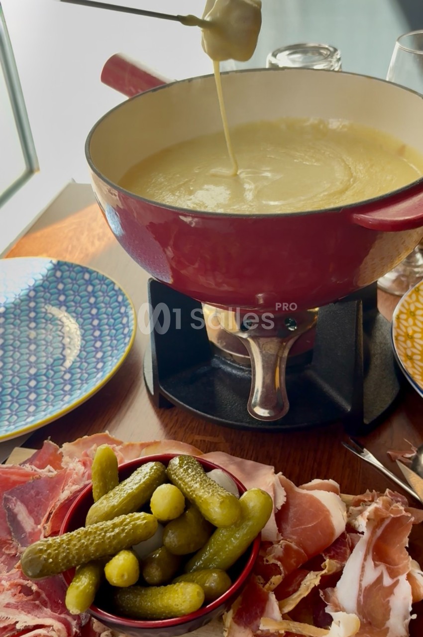 Caquelon de fondue au fromage avec cornichons, charcuterie et assiettes colorées sur une table en bois.