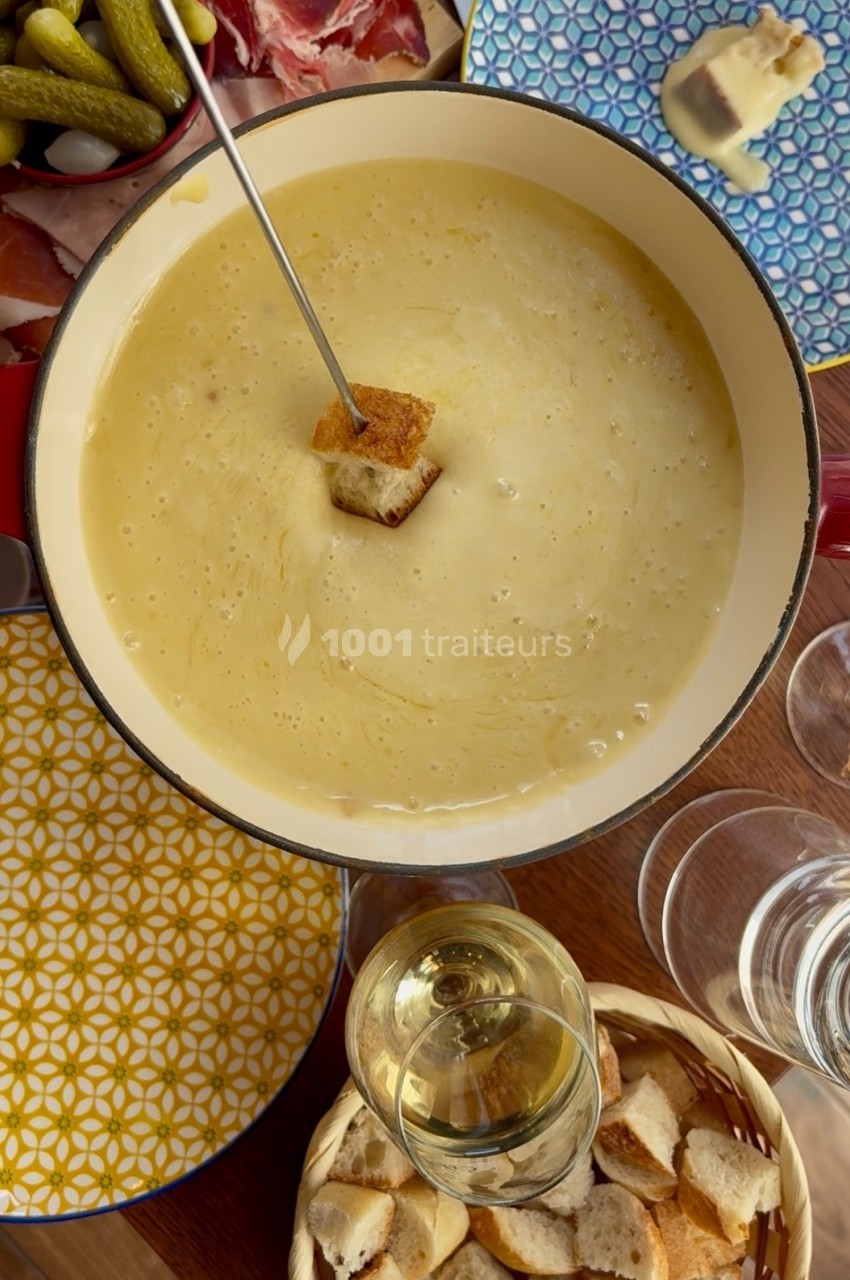Fondue au fromage dans une casserole, avec un morceau de pain trempé sur une fourchette, entourée d'accompagnements.