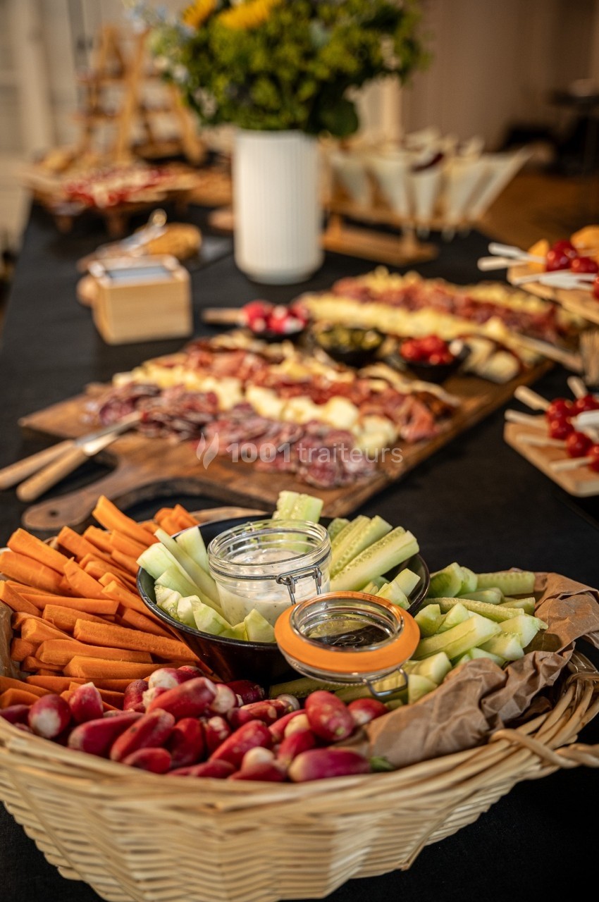 Plateau de légumes frais avec carottes, radis et concombres, accompagné de sauces, sur une table de buffet.