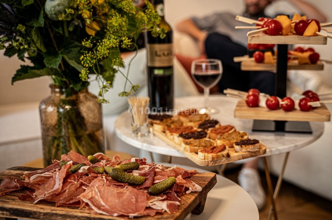 Plateau de charcuterie avec cornichons, toasts variés, brochettes apéritives et bouteille de vin sur une table basse.