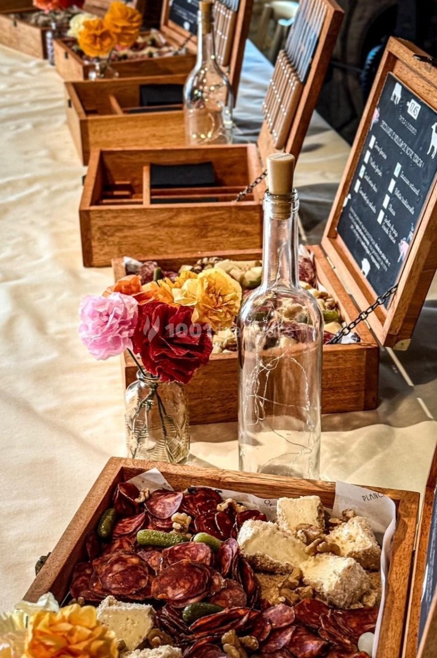 Plateaux en bois garnis de charcuterie, fromages et cornichons, disposés sur une table avec des fleurs et une bouteille en…