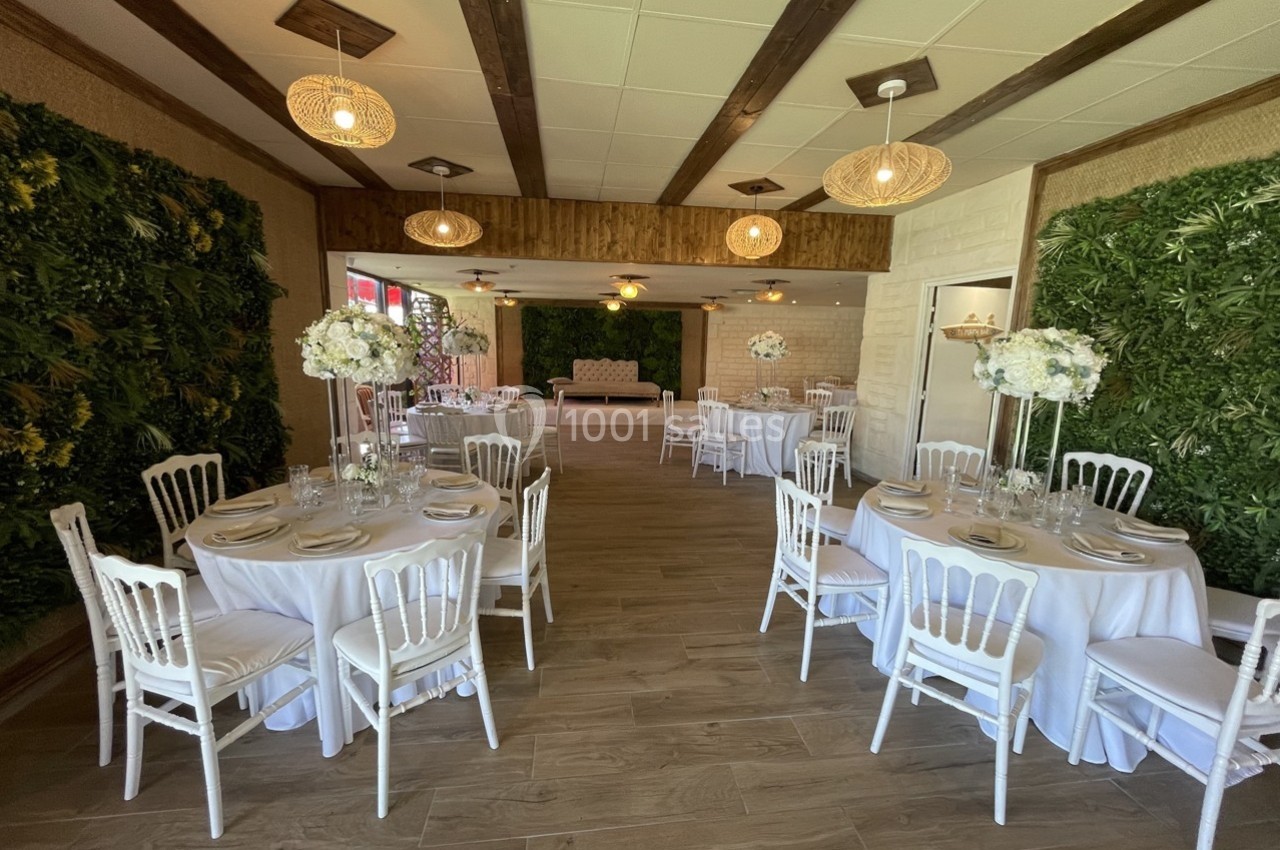 Salle de réception décorée avec des tables rondes, nappes blanches, chaises élégantes et murs ornés de végétation.