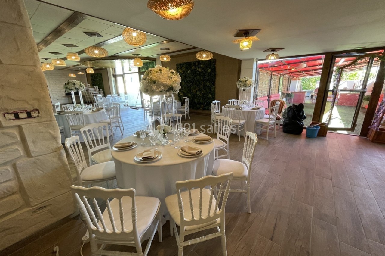 Salle de réception décorée avec des tables rondes, nappes blanches, chaises élégantes et compositions florales.