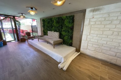 Entrée d'un bâtiment beige avec une toiture rouge, entourée de palissades en bois et d'une pelouse artificielle.