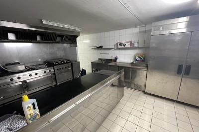 Entrée d'un bâtiment beige avec une toiture rouge, entourée de palissades en bois et d'une pelouse artificielle.