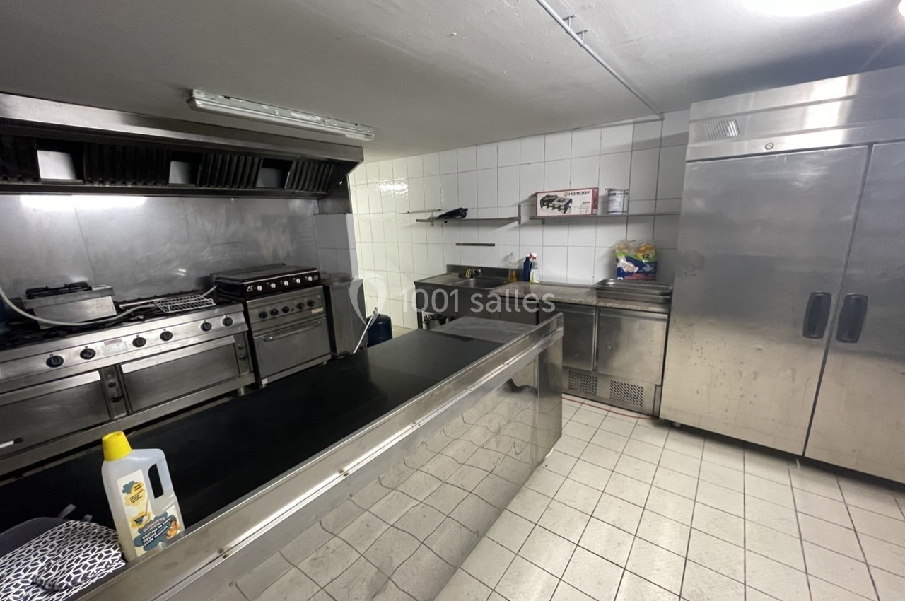 Cuisine professionnelle avec équipements en inox, comprenant un four, des plaques de cuisson et un réfrigérateur.